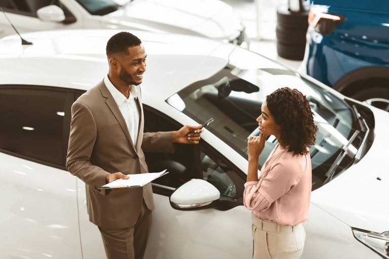Car Sales Manager Showing Auto To Lady Standing In Dealership