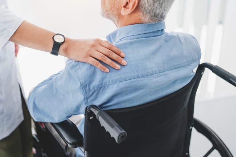 Close up of medical worker supporting disabled old mature man sitting in wheelchair