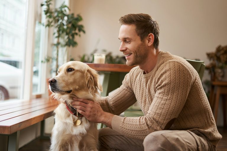 Portrait of young handsome dog-owner, spending time with his pet in a cafe, sitting indoors