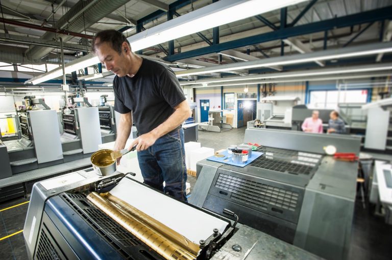 Worker applying gold ink to printing machine in print workshop