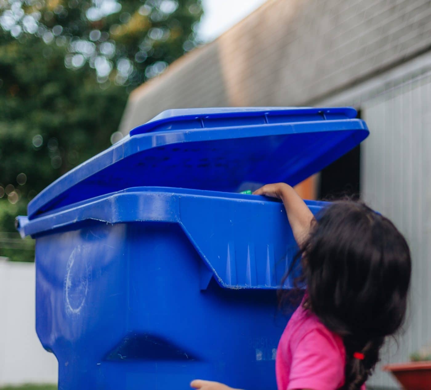 Diverse pre school girl putting can into blue recycling bin