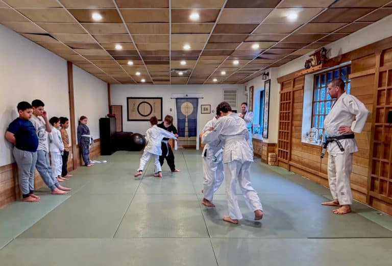 OM Brazilian Jiu‑Jitsu Free Youth Class: Sensei Milard Roper supervises 2 pairs of students grappling.