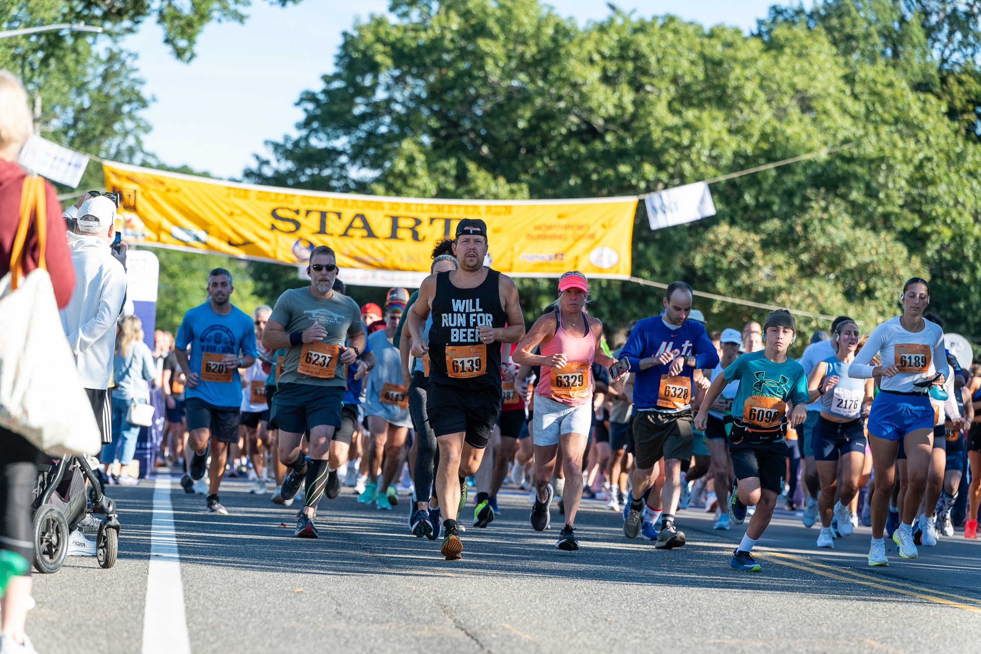 The Great Cow Harbor 10K Run 2025: A large group of runners take off from the starting line.
