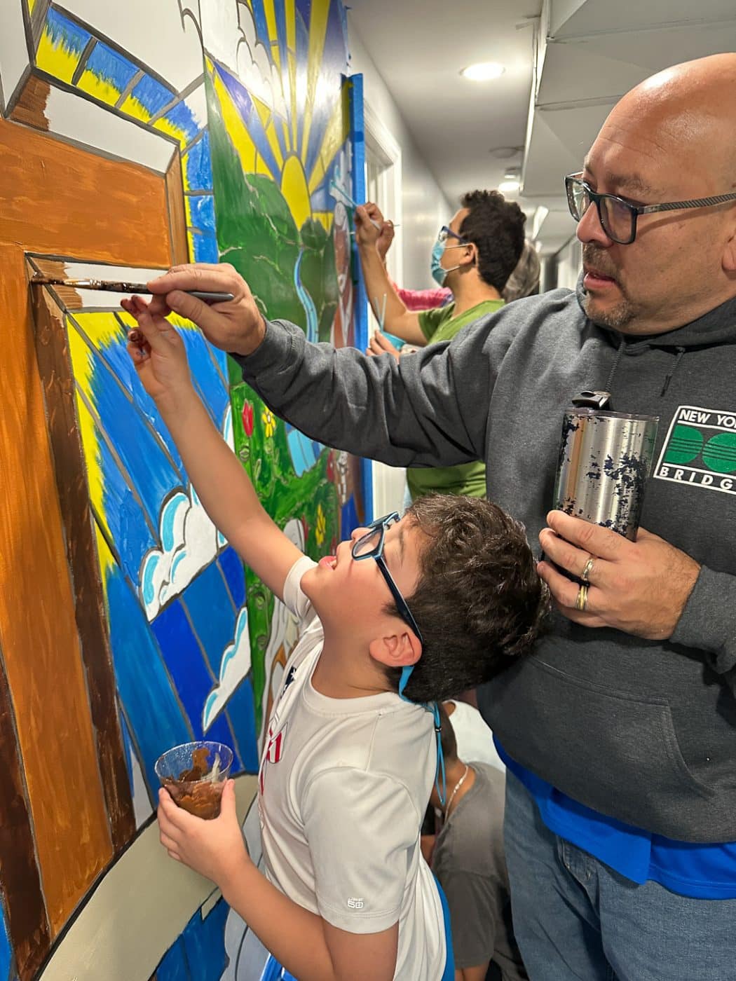Father and son paint the mural at Assembly of God. Faith and Blue 2025