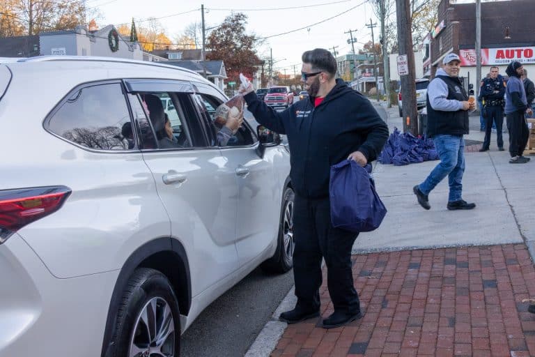 Volunteer passes a frozen turkey through a car window with a donated bag of fixings. Sorrentino Turkey Giveaway 2025