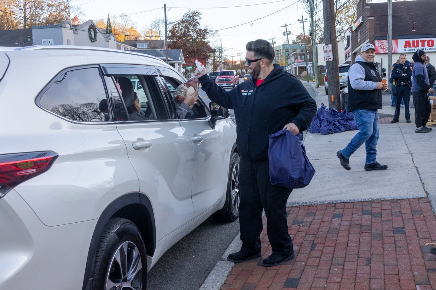 Volunteer passes a frozen turkey through a car window with a donated bag of fixings. Sorrentino Turkey Giveaway 2025