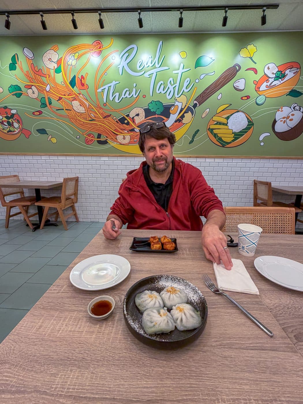 Lance Margolin - the last moment he hated Thai food. Man sitting at restaurant table with an appetizer in front of him and a colorful thai food mural behind him. Raan Thai Opens in Huntington Station - And It Changed His Mind About Thai Food