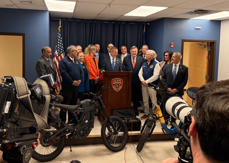 Suffolk County Police Commissioner Kevin Catalina with Town of Huntington Legislators Stephanie Bontempi (orange) and Rebecca Sanin (bright blue) together with officials with illegal e-bikes. Suffolk County Enforces New E-Bike and E-Scooter Laws Focused on Safety