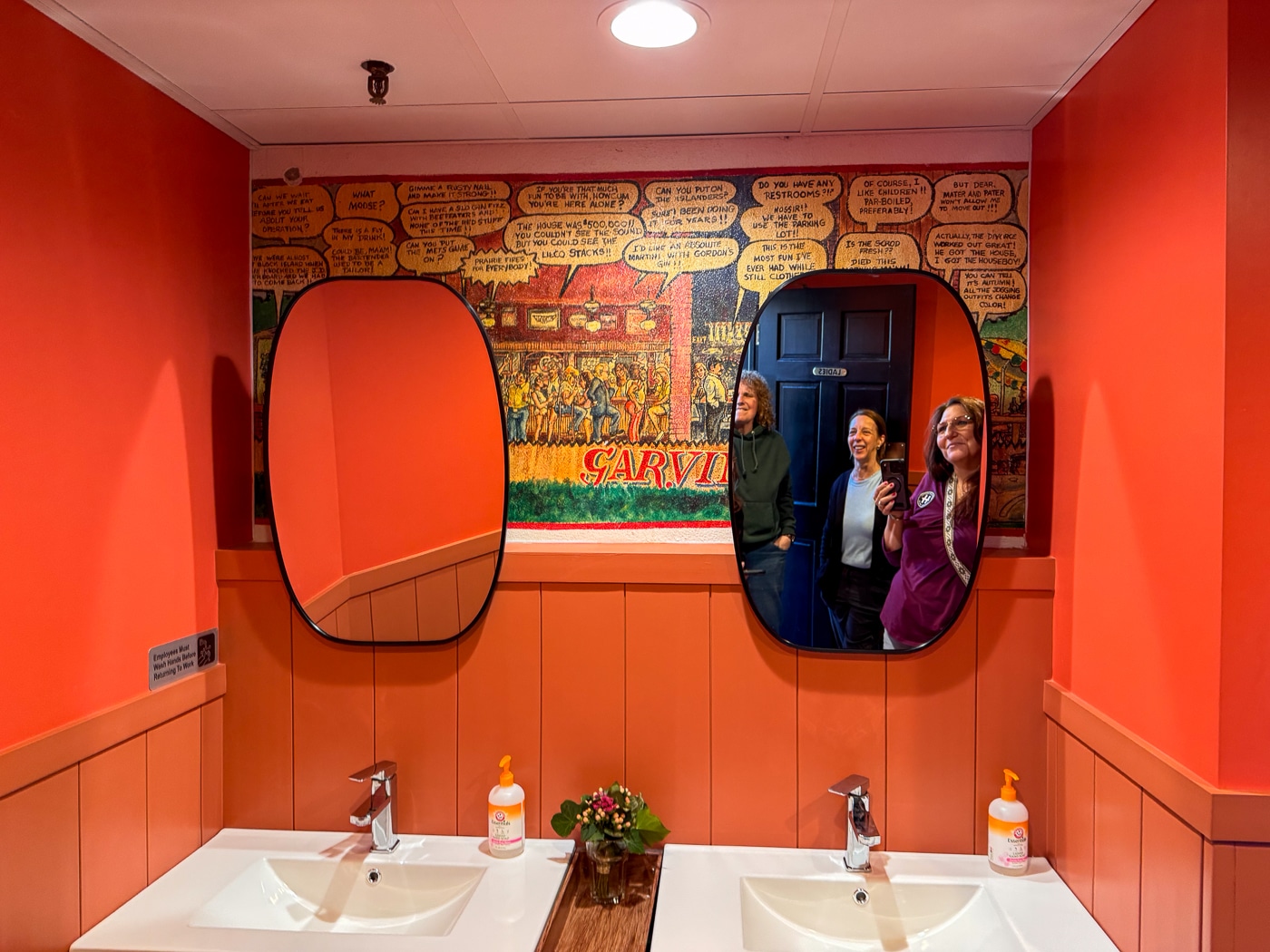 Owner Daria Lamb, center, reveals their preservation of a Huntington landmark - the Garvin's mural of 1980s regulars and their conversations in the ladies room. Daria redesigned the bathroom to complement the historic mural. With Dana Richter and June Margolin, Huntington Matters. A Slice of Nostalgia Meets Something New at Mighty Fine