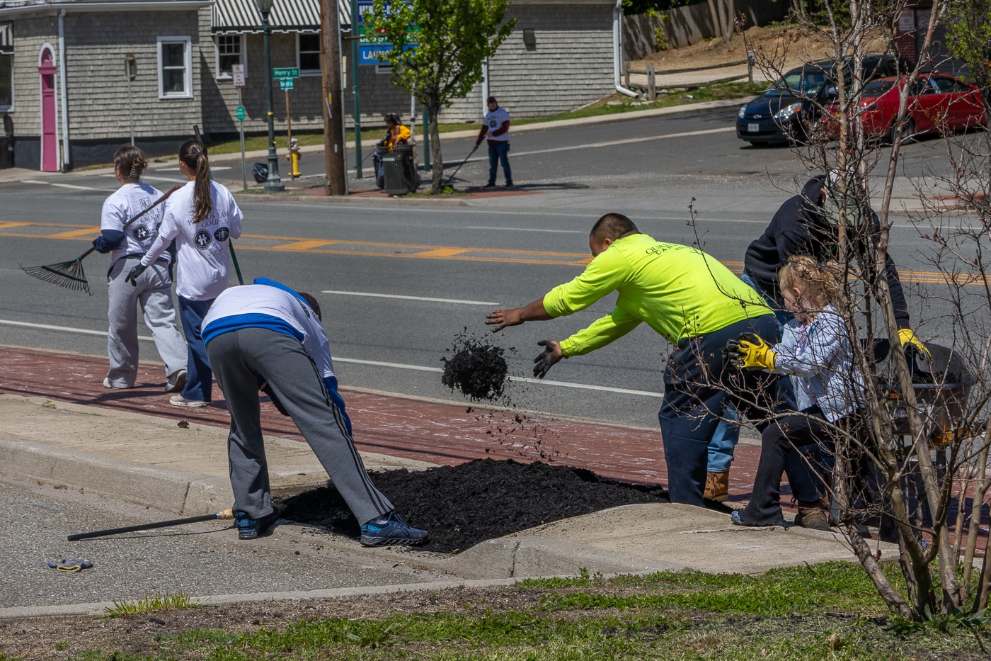 A Quality Island Landscaping crew member tosses mulch on a garden bed with Owner John Marcinka, Jr. and daughter Luna at right and a team of volunteers on both sides of New York Avenue cleaning. Huntington Station Latin Quarter and Huntington Matters Host 16th Annual Spring Cleanup